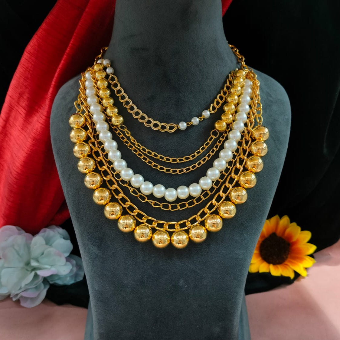 Gold and pearl necklace on a mannequin bust with flowers in the background